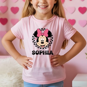 A young girl wearing a pink t-shirt with a Minnie Mouse design and the name "Sophia" printed on it.