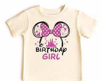 May include: Cream-colored t-shirt featuring a Minnie Mouse-inspired design. The graphic includes a pink polka-dot bow, black mouse ears, a pink castle, and the words "BIRTHDAY GIRL" in black and pink.