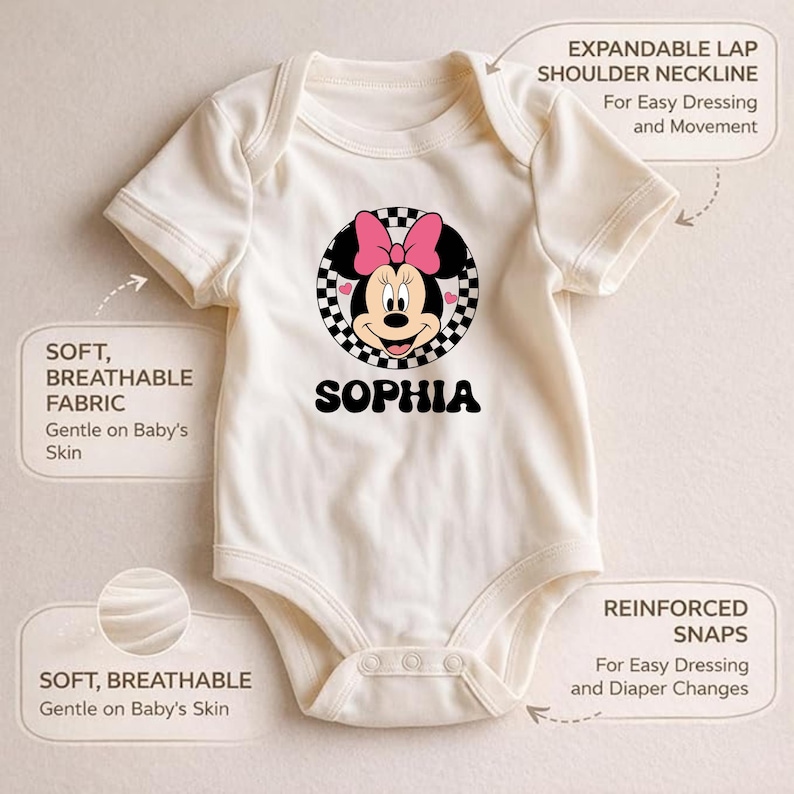 a white onesie with a Minnie Mouse design and the name "Sophia" printed on it. The onesie has several features, including an expandable shoulder strap, a soft and breathable fabric, gentle on baby's skin, and reinforced snaps for easy dressing and diaper changes.