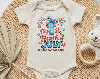 Puede incluir: Un body de bebé de manga corta en color crema con un estampado gráfico que dice My 1st Fourth of July en letras rojas y azules. El diseño incluye un número uno azul con un lazo, estrellas rojas y azules y detalles de fuegos artificiales.