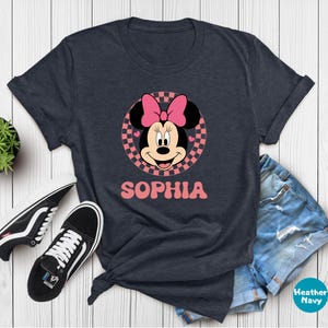 A gray t-shirt with a Minnie Mouse graphic and the name "Sophia" printed on it, along with a pair of jeans and black and white sneakers.