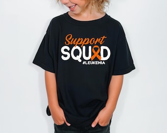 May include: A black short-sleeved t-shirt featuring the orange and white text Support SQUAD with an orange awareness ribbon replacing the letter A. Below the main text, the word #LEUKEMIA is printed in white capital letters.