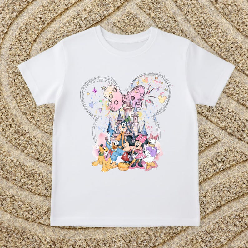 A white t-shirt with a colorful graphic design featuring Disney characters Mickey Mouse, Donald Duck, and Goofy, along with a castle and other whimsical elements.