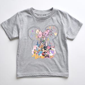 A gray t-shirt with a colorful graphic design featuring Disney characters such as Mickey Mouse, Donald Duck, Goofy, and Minnie Mouse, along with a castle and fireworks in the background.