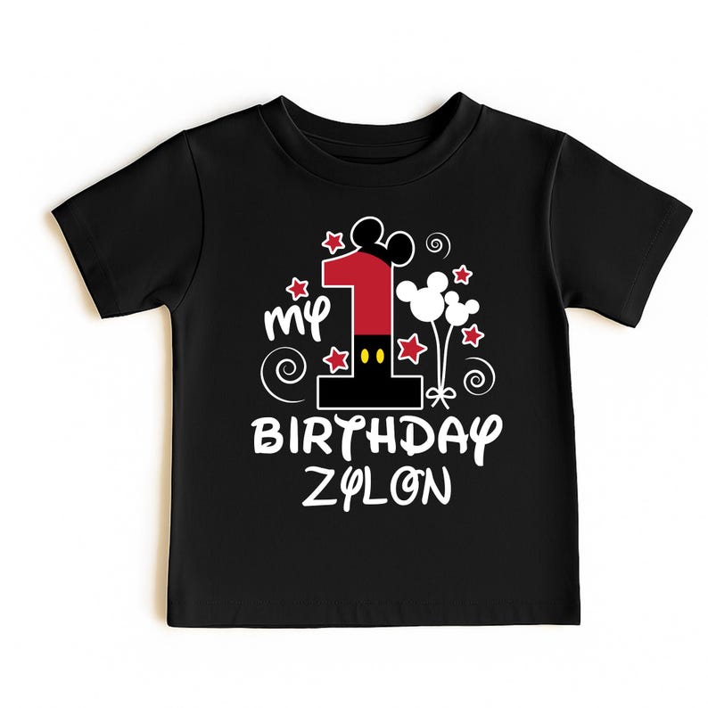 K&ouml;nnte beinhalten: Schwarzes Kleinkind-T-Shirt mit einer farbenfrohen Grafik zum ersten Geburtstag. Das Design umfasst eine gro&szlig;e rote Zahl 1, Mickey Mouse Ohren, Sterne und den Text "My Birthday Zylon."