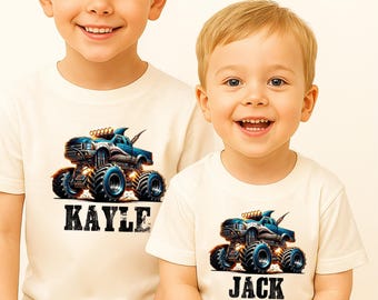 May include: Two children wearing off-white t-shirts with a monster truck graphic. The blue and orange monster truck design is on the front of the shirts. One shirt says "KAYLE" and the other says "JACK" in black block letters.