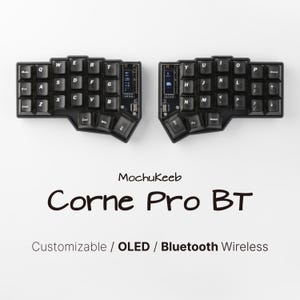 Peut inclure: Un clavier ergonomique divisé noir avec des touches noires, doté d'écrans OLED sur chaque moitié. Le texte MochuKeeb Corne Pro BT Customizable / OLED / Bluetooth Wireless est imprimé sous les moitiés du clavier sur un fond blanc uni.