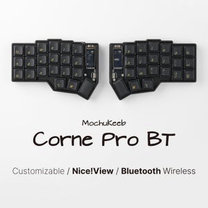 Peut inclure: Un clavier ergonomique divisé noir en deux parties, doté de touches sombres avec des lettres dorées, de petits écrans intégrés et le texte MochuKeeb Corne Pro BT Customizable / Nice!View / Bluetooth Wireless imprimé en dessous.