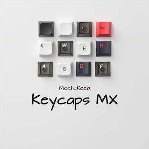 Può includere: Disposizione di dodici tasti di tastiera in vari colori e design, tra cui nero, bianco e rosso. I tasti sono disposti a griglia su sfondo bianco. Il testo "MochuKeeb Keycaps MX" è visualizzato sotto.