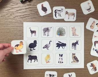 May include: A set of farm animal flashcards with illustrations of various animals, including a duckling, donkey, and owl. A hand holds a duckling card. A toy tractor and a basket are also visible.