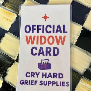 Puede incluir: Una tarjeta blanca con el texto "OFFICIAL WIDOW CARD" en morado y rojo, con una estrella y un gráfico de caja de pañuelos. El texto "CRY HARD GRIEF SUPPLIES" está debajo. La tarjeta está en una funda de plástico transparente.
