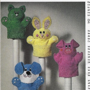 Peut inclure: Instructions pour la fabrication de marionnettes en tissu éponge. Les instructions comprennent le traçage de patrons, l'ajout de détails en tissu et la couture des marionnettes. L'image montre quatre marionnettes : une grenouille verte, un lapin jaune, un cochon rose et un chien bleu.