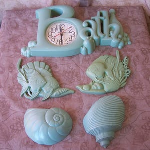 May include: A set of aqua blue plastic wall decor featuring a clock, the word "Bath", two fish, a seashell, and a snail. The clock has a white face with black numbers and hands.