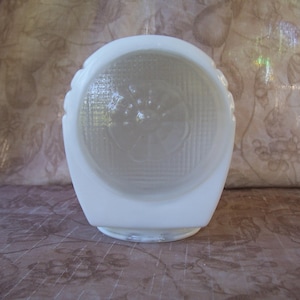 May include: A white, vintage-style glass light fixture with a textured, patterned front. The fixture has a rounded top and a square base. The glass has a floral design in the center. The fixture is likely for a ceiling or wall.