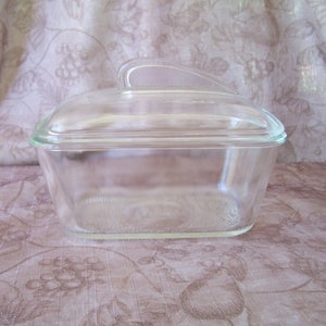 May include: A clear glass rectangular baking dish with a lid and a handle on the lid. The dish is empty.