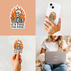 May include: A sticker featuring a cartoon skeleton giving a thumbs up while engulfed in flames. The text "IT'S FINE. I'M FINE." is below the skeleton. The sticker is shown on a phone, laptop, and held by a person.