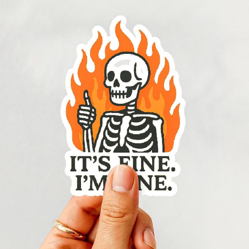May include: A white sticker featuring a cartoon skeleton giving a thumbs up, set against a backdrop of orange flames. The text "IT'S FINE. I'M FINE." is printed below the skeleton in black.