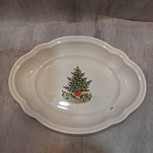 May include: An oval-shaped cream-colored ceramic serving platter with a scalloped edge. The center of the platter features a colorful illustration of a decorated Christmas tree with a toy train set circling the base on a green grassy patch.