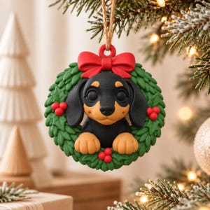 May include: A round Christmas ornament featuring a sculpted black and tan dachshund puppy peeking through a green holly wreath. The ornament is topped with a bright red bow and hangs from a rustic twine loop, showcasing detailed textures.