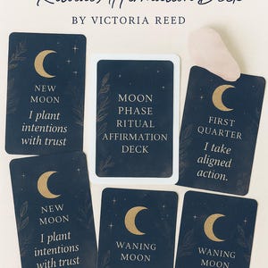 May include: A Moon Phase Ritual Affirmation Deck with navy blue cards featuring gold crescent moons and botanical illustrations. The deck includes affirmations for each moon phase, with text such as "I plant intentions with trust."