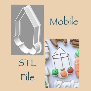 May include: A white 3D printed cookie cutter shaped like a mobile, labeled STL File and Mobile. Next to it is a decorated cookie featuring a white mobile frame with brown lines and three hanging items: a green leafy vegetable, a peach, and a red tomato.