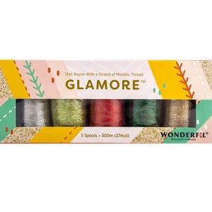 May include: A box set of five spools of GLAMORE™ thread, each with a strand of metallic thread. The spools are silver, gold, red, green, and bronze. The box has a glittery gold and colorful design. Each spool contains 300m (274yd) of thread.