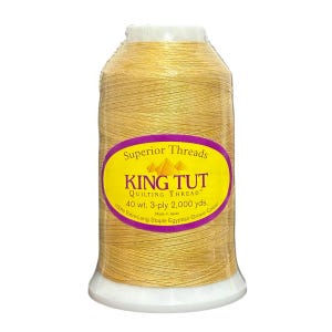 May include: A spool of King Tut quilting thread in a golden yellow color. The label reads "Superior Threads" and "40 wt. 3-ply 2,000 yds." Made from 100% Extra-Long Staple Egyptian-Grown Cotton. The spool is wrapped in clear plastic.