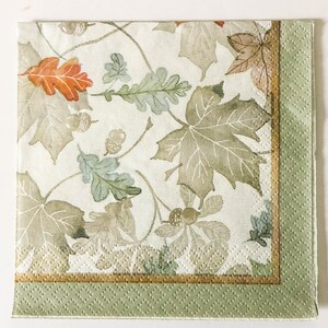 May include: A white paper napkin with a green border and a gold trim. The napkin features a watercolor-style pattern of leaves in shades of brown, green, and orange.