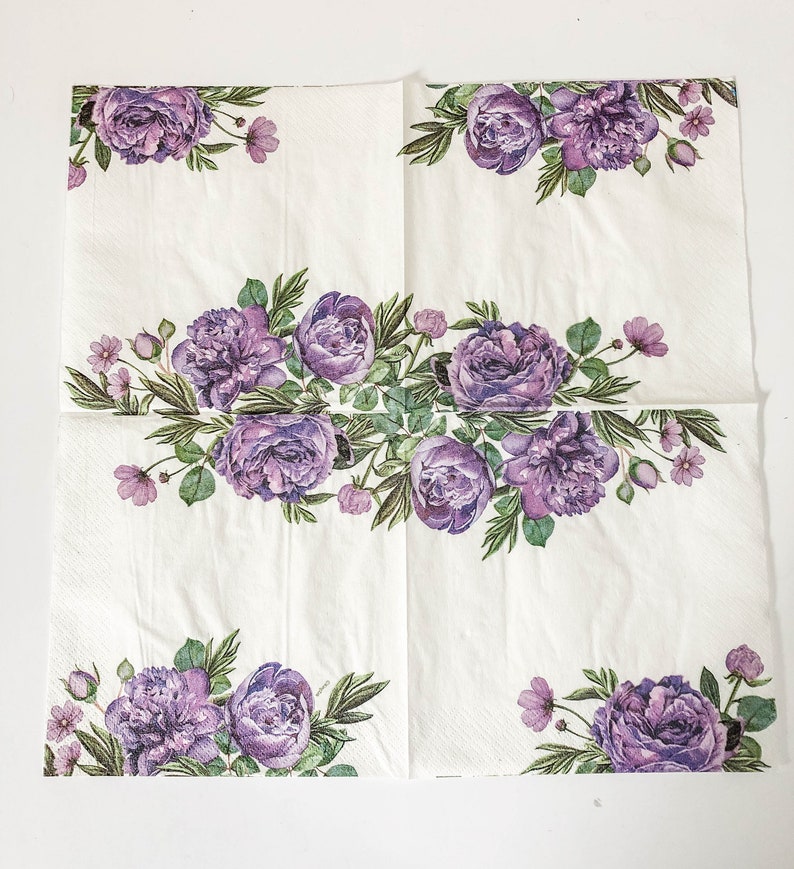 Puede incluir: Servilletas de papel blancas con un dise&ntilde;o floral morado. El dise&ntilde;o presenta un borde de flores y hojas moradas alrededor de los bordes de la servilleta. El centro de la servilleta presenta un dise&ntilde;o floral m&aacute;s grande con flores y hojas moradas.
