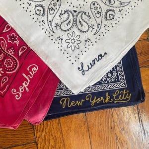 May include: Three bandanas with paisley patterns. One is red with "Sophia" embroidered in white, another is white with "Luna" embroidered in blue, and the third is navy blue with "New York City" embroidered in gold.