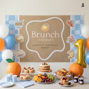 May include: A brunch-themed birthday party setup featuring a large banner with the text Brunch ANYONE? HAPPY 1ST BIRTHDAY PENNY, surrounded by illustrations of breakfast foods, balloons, orange-shaped decor, and a table with pancakes and fruit.
