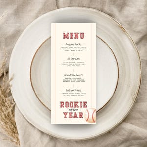 Puede incluir: Una tarjeta de menú rectangular vertical con fondo crema y texto rojo. El encabezado dice MENU, seguido de secciones para Pregame Snacks, All-Star Eats, Grand Slam Sweets y Ballpark Drinks. El texto inferior dice ROOKIE of the YEAR con una pelota de béisbol.