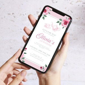May include: A smartphone displays a pink and white invitation for Olivia's 1st birthday tea party. The design includes floral accents, a teapot illustration, and the text "Let's Par Tea!" and "Olivia's 1st birthday". The date is April 15th, 2028.
