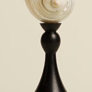 Op de afbeelding: Een decoratieve schelpenbeeldhouwwerk. De sculptuur heeft een grote, parelmoer schelp bovenop een donkerhouten standaard. De standaard heeft een bolvormig middengedeelte en een uitlopende basis, wat een opvallend contrast cre&euml;ert.
