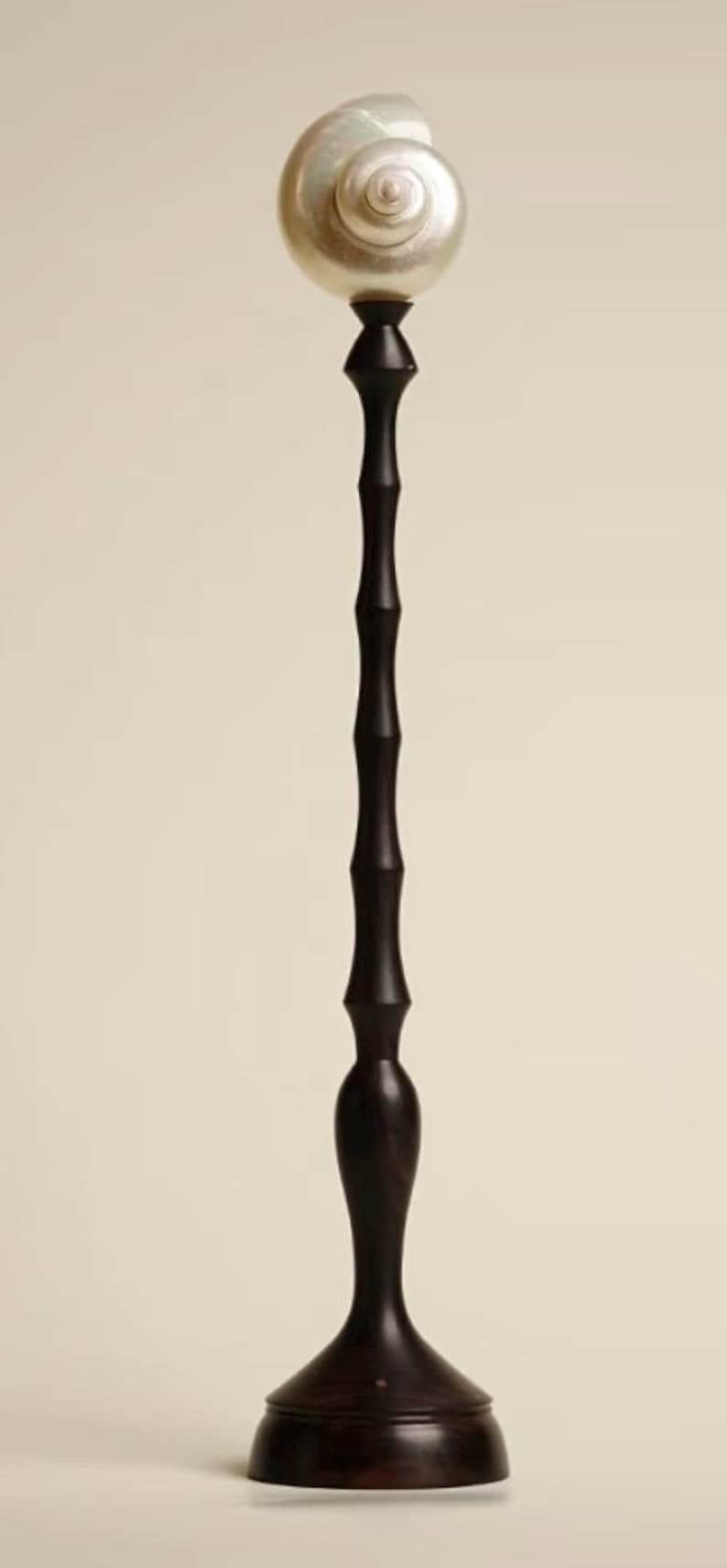 Op de afbeelding: Een hoog, donkerbruin decoratief object met een parelmoer, spiraalvormige top. De steel is een reeks verbonden, cilindrische vormen. De basis is een uitlopende, afgeronde vorm. Het object staat tegen een neutrale achtergrond.