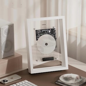 May include: A white framed display featuring a CD and circuit board. The CD is white with text. The frame is on a desk with a speaker and a phone. The text "CoolDesk" is visible on the frame.