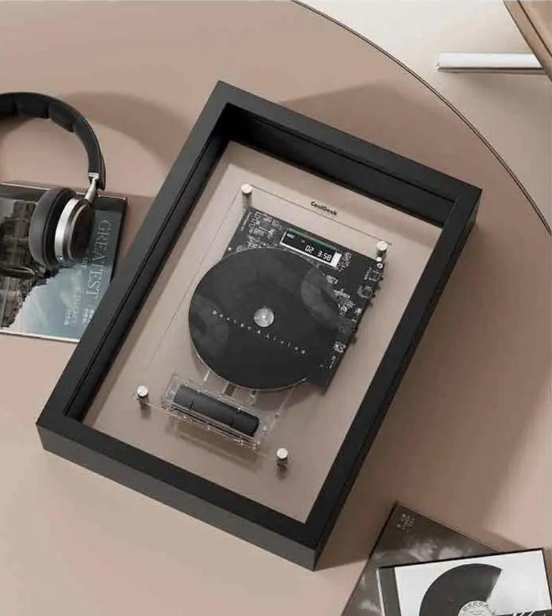 May include: A black framed display featuring a black CD and circuit board design. The CD is mounted on a clear acrylic panel. The frame is rectangular and sits on a light brown surface. The text "CoolDesk" is visible.
