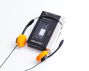May include: A vintage Sony Walkman cassette player with a black and silver body, paired with orange and black headphones. The Walkman is labeled with the Sony and Walkman logos. The headphones are connected to the player with a black wire.