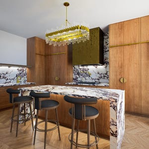 Può includere: Una cucina moderna con un'isola con piano in marmo e paraschizzi abbinato. La cucina presenta mobili in legno, una cappa dorata e un lampadario dorato. Sgabelli da bar neri sono posizionati attorno all'isola. Una scala in legno è appoggiata ai mobili.