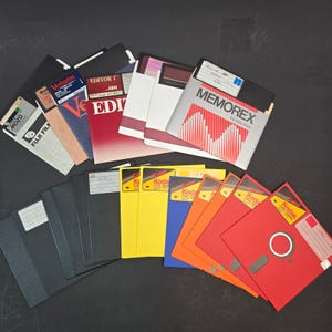 Puede incluir: Una colección de disquetes de 3,5 pulgadas en varios colores, incluyendo negro, amarillo, azul, naranja y rojo. Las marcas incluyen Memorex, Kodak, Verbatim y Fuji Film. Algunos disquetes presentan etiquetas escritas a mano y texto impreso.