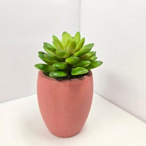 Puede incluir: Una taza de cerámica blanca con asa negra y el texto "But First, Coffee" en negrita negra. La taza se encuentra sobre un fondo borroso, sugiriendo un ambiente acogedor.