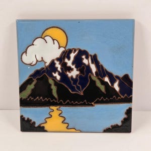 Könnte beinhalten: Quadratische Keramikfliese mit einer Berglandschaft. Das Design zeigt einen blauen Himmel, eine gelbe Sonne, eine weiße Wolke und eine Bergkette mit schneebedeckten Gipfeln, die sich in einem blauen See spiegeln. Die Fliese hat eine glänzende Oberfläche und einen braunen Rand.