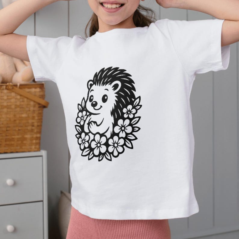 May include: White t-shirt with a black and white illustration of a hedgehog encircled by flowers. The hedgehog has a cheerful expression. The shirt is made of a soft material.
