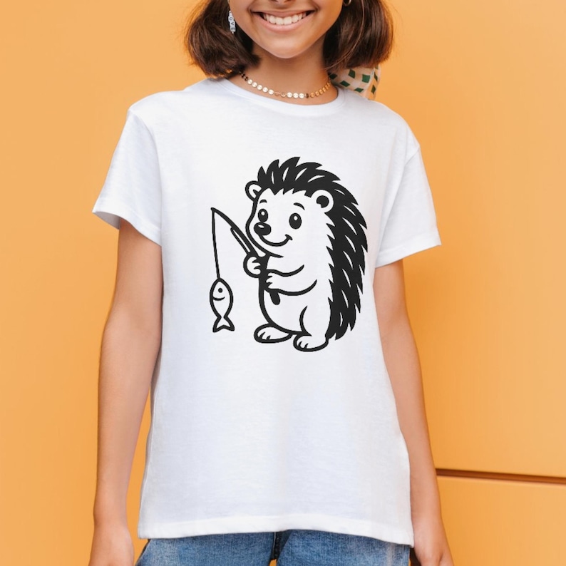 May include: White t-shirt with a black and white cartoon hedgehog fishing. The hedgehog is depicted with a fishing rod and a fish. The t-shirt has a round neck and short sleeves, a casual style.