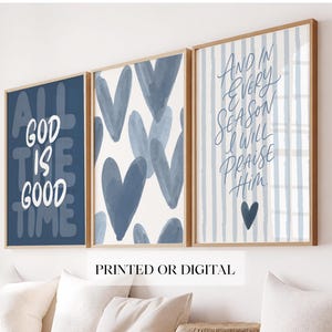 Könnte beinhalten: Ein Set aus drei gerahmten Wandbildern. Das linke Bild ist dunkelblau mit weißem Text ALL GOD IS GOOD TIME. Das mittlere Bild zeigt ein Muster aus blauen Herzen auf weißem Grund. Das rechte Bild hat blaue Streifen und den Text AND IN EVERY SEASON I WILL PRAISE HIM mit einem kleinen blauen Herz.