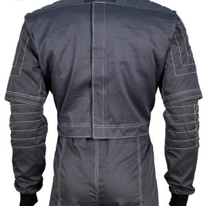 Puede incluir: Mono gris oscuro con costuras blancas. Vista trasera que muestra el cuello, el acolchado de los hombros y las mangas con l&iacute;neas de costura horizontales. El mono tiene pu&ntilde;os negros y una costura blanca vertical en el centro.