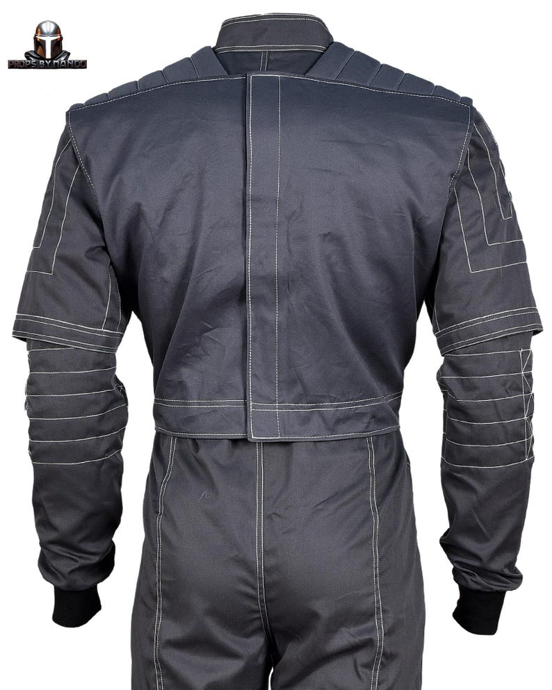 Puede incluir: Mono gris oscuro con costuras blancas. Vista trasera que muestra el cuello, el acolchado de los hombros y las mangas con l&iacute;neas de costura horizontales. El mono tiene pu&ntilde;os negros y una costura blanca vertical en el centro.