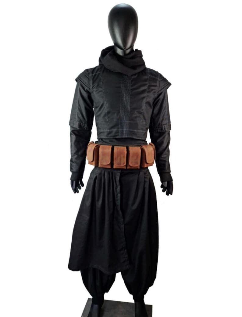 May include: A black outfit consisting of a long-sleeved top with a high collar, a matching hood, and loose-fitting trousers. A brown leather utility belt with five rectangular pouches is worn around the waist over the black fabric ensemble.