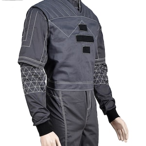 Puede incluir: Mono gris con costuras blancas y detalles negros. La parte superior presenta un cuello alto, patrones geom&eacute;tricos y parches negros. Las mangas tienen un dise&ntilde;o geom&eacute;trico &uacute;nico en la parte superior del brazo y los pu&ntilde;os son negros.