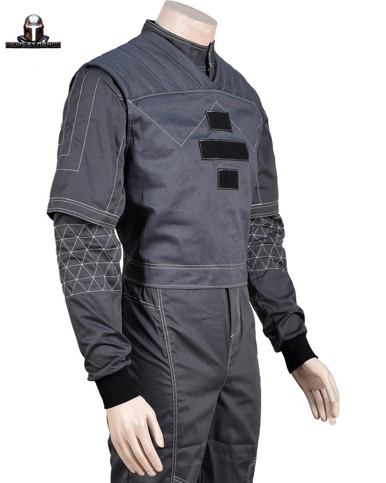 Puede incluir: Mono gris con costuras blancas y detalles negros. La parte superior presenta un cuello alto, patrones geom&eacute;tricos y parches negros. Las mangas tienen un dise&ntilde;o geom&eacute;trico &uacute;nico en la parte superior del brazo y los pu&ntilde;os son negros.